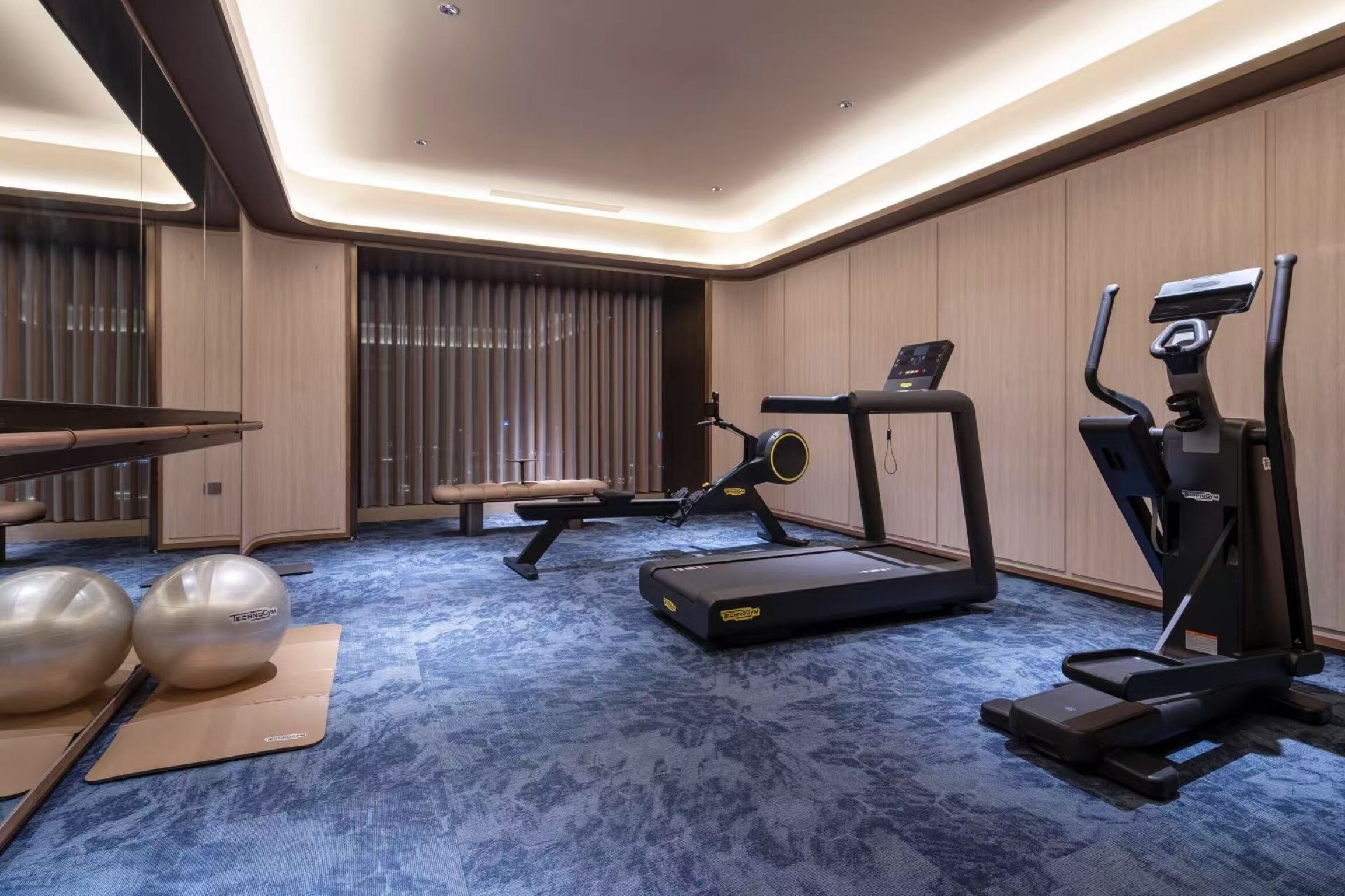 Un gimnasio moderno con equipo de ejercicio, una banca y suelo cubierto de moqueta azul.