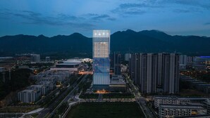 A modern high-rise building with a unique vertical design, surrounded by other high-rise buildings and a mountainous backdrop. - Orange Crystal Hangzhou Tonglu Station (Hangzhou)