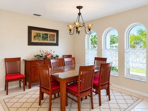 A dining room with a glass table, wooden chairs, a chandelier, and a framed artwork on the wall. - 3BR Canal Home with Pool, Dock & Pool Table (Port Charlotte)