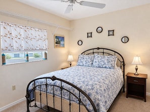 A bedroom with a bed, two bedside tables, a window with curtains, a ceiling fan, and wall-mounted mirrors. - 3BR Canal Home with Pool, Dock & Pool Table (Port Charlotte)