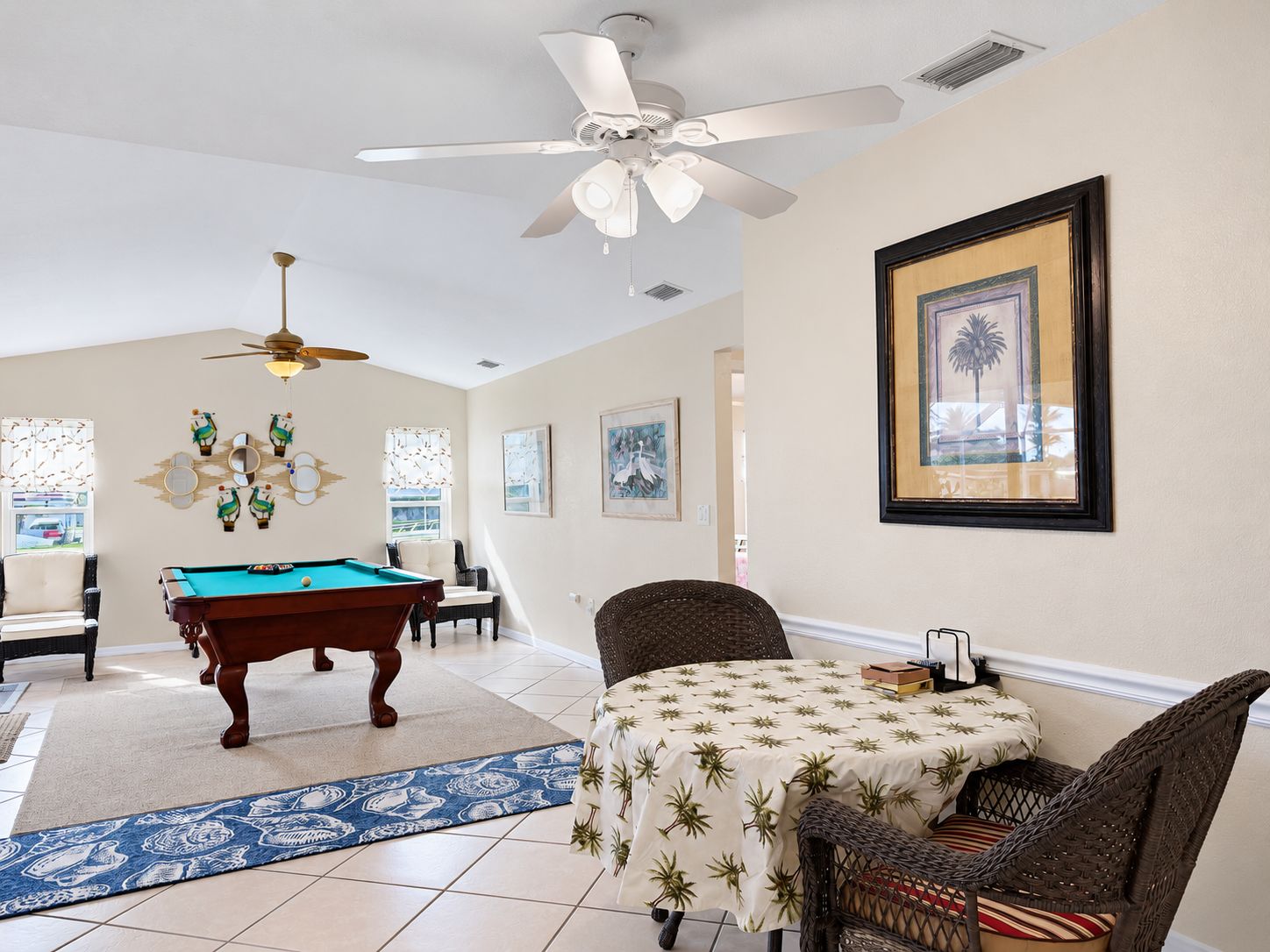 A room with a pool table, a ceiling fan, a table with a patterned tablecloth, and framed artwork on the wall.