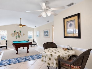 A room with a pool table, a ceiling fan, a table with a patterned tablecloth, and framed artwork on the wall. - 3BR Canal Home with Pool, Dock & Pool Table (Port Charlotte)