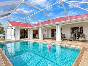Ein Schwimmbecken mit Glasüberdachung, rotem Dach und Liegestühlen.