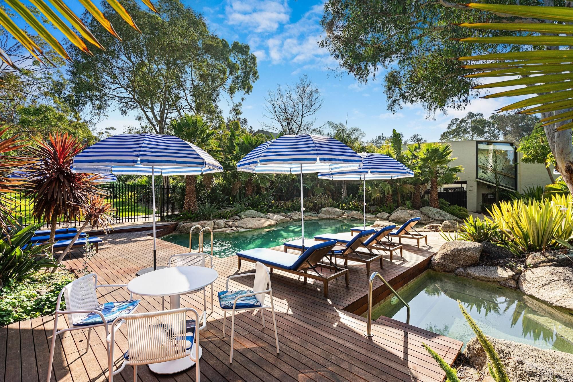 Een zwembadgedeelte met ligbedden, parasols en een houten terras.