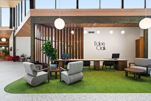 Un espacio de oficina moderno con un escritorio de madera, dos sillones grises, una mesa redonda y una planta en maceta.
