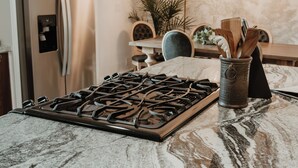 Eine Küche mit Gasherd, Kühlschrank, Esstisch mit Stühlen und einer Pendelleuchte.