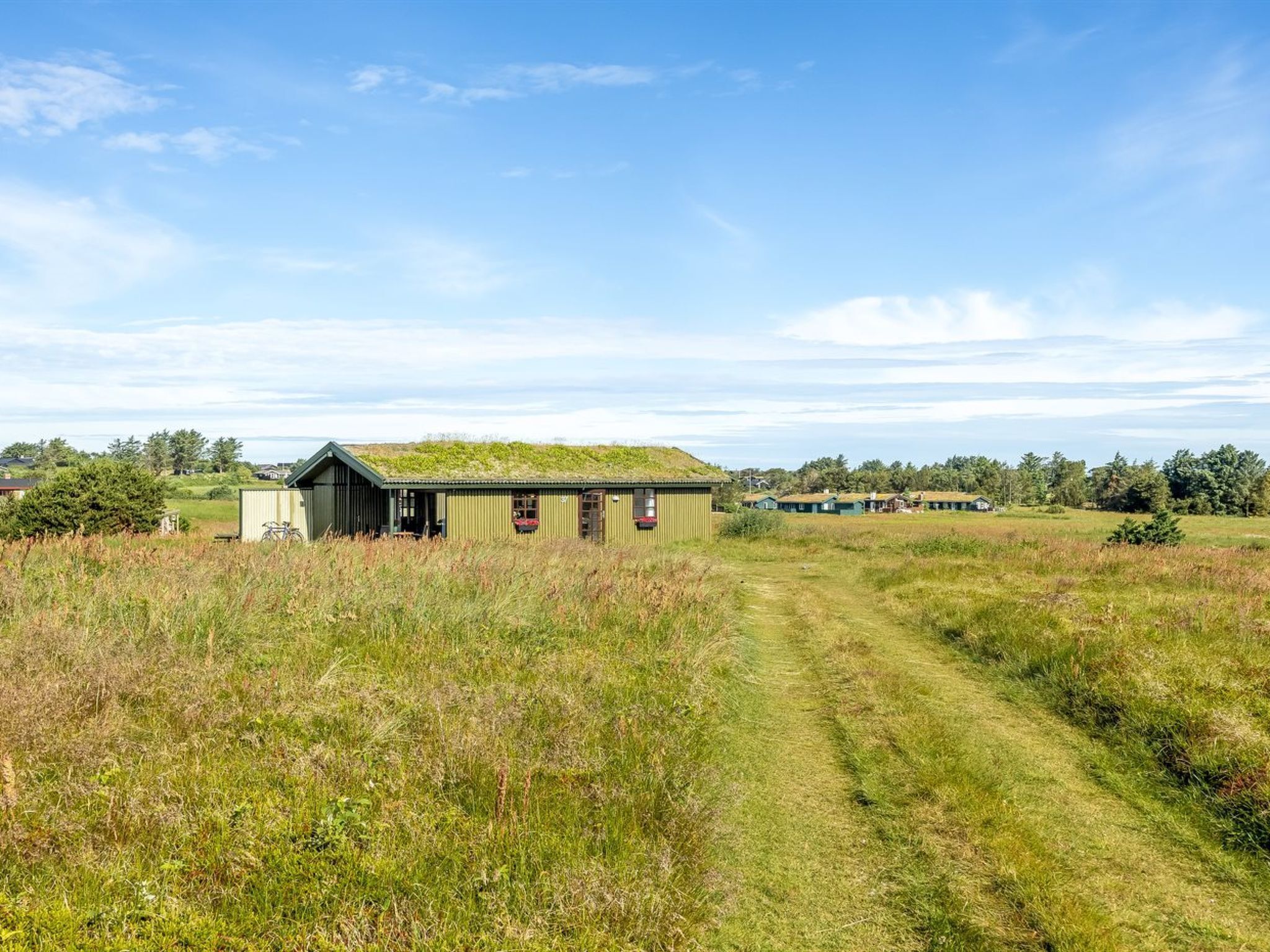A rural setting with a small building, a dirt path, and distant houses.