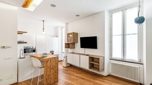 Une cuisine moderne avec un îlot central en bois, des meubles blancs et un téléviseur encastré.