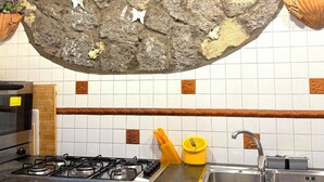 Eine Küche mit Steinwand, weißen Fliesen, einem Gasherd und weißen Schränken.