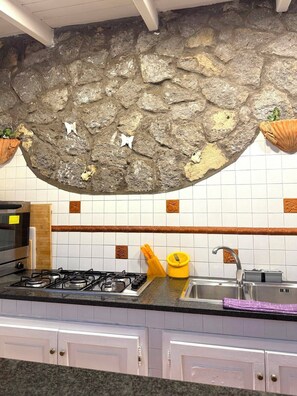 A kitchen with a stone wall, white tiles, a gas stove, and white cabinets. - Villa San Francesco Garden (Forio d'Ischia)