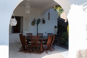 An outdoor dining area with a table and chairs, surrounded by a white wall with decorative lanterns and a stone wall with plants. - Villa San Francesco Garden (Forio d'Ischia)