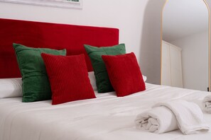 A bed with white bedding and red and green pillows, a white headboard, and a white wall with a framed picture. - Villa San Francesco Garden (Forio d'Ischia)