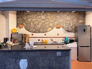 A modern kitchen with a stone accent wall, a central island, and stainless steel appliances. - Villa San Francesco Garden (Forio d'Ischia)