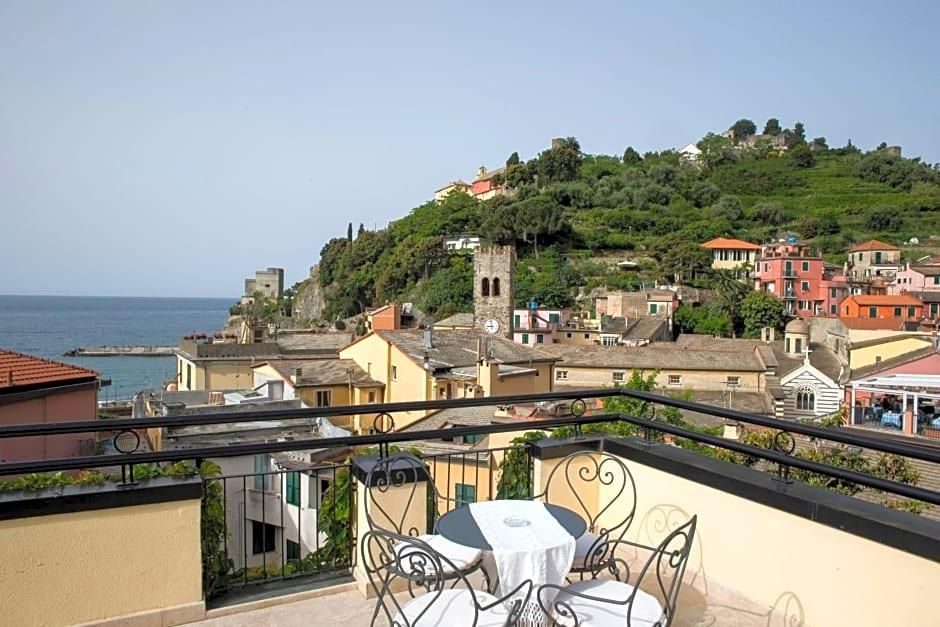 Un balcone con tavolo e sedie, affacciato su una cittadina costiera con edifici e una collina.