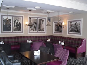 A restaurant with a long bench seating area, tables, and pendant lighting. - The Horse And Hound Inn Hotel (Ballynabola)