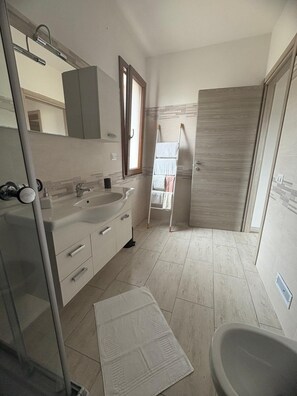 Un bany amb rentatge, mirall, paraigua de tovalloles i zona de dutxa.