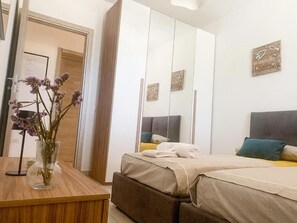 Une chambre à coucher avec un lit, une table de chevet ornée d’un vase, une armoire et un miroir.