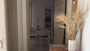 Käytävällä on puinen vastaanottotiski, maljakko, jossa on kuivattuja kasveja, ja seinällä on kehystetty kuva.