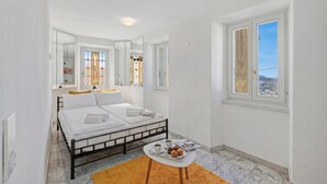 Ein Schlafzimmer mit einem Bett, einem kleinen Tisch mit einem Tablett voller Muffins, einem Fenster mit Blick und einem Spiegel, der den Raum reflektiert.