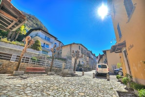 Una calle adoquinada con una banca, coches estacionados y edificios con balcones.