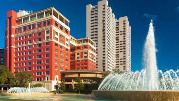 Un hotel con fachada roja, varios pisos y una fuente al frente.