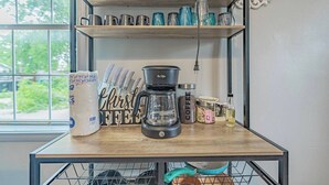 Una encimera de cocina con una cafetera, recipientes de café y un paquete de azúcar.