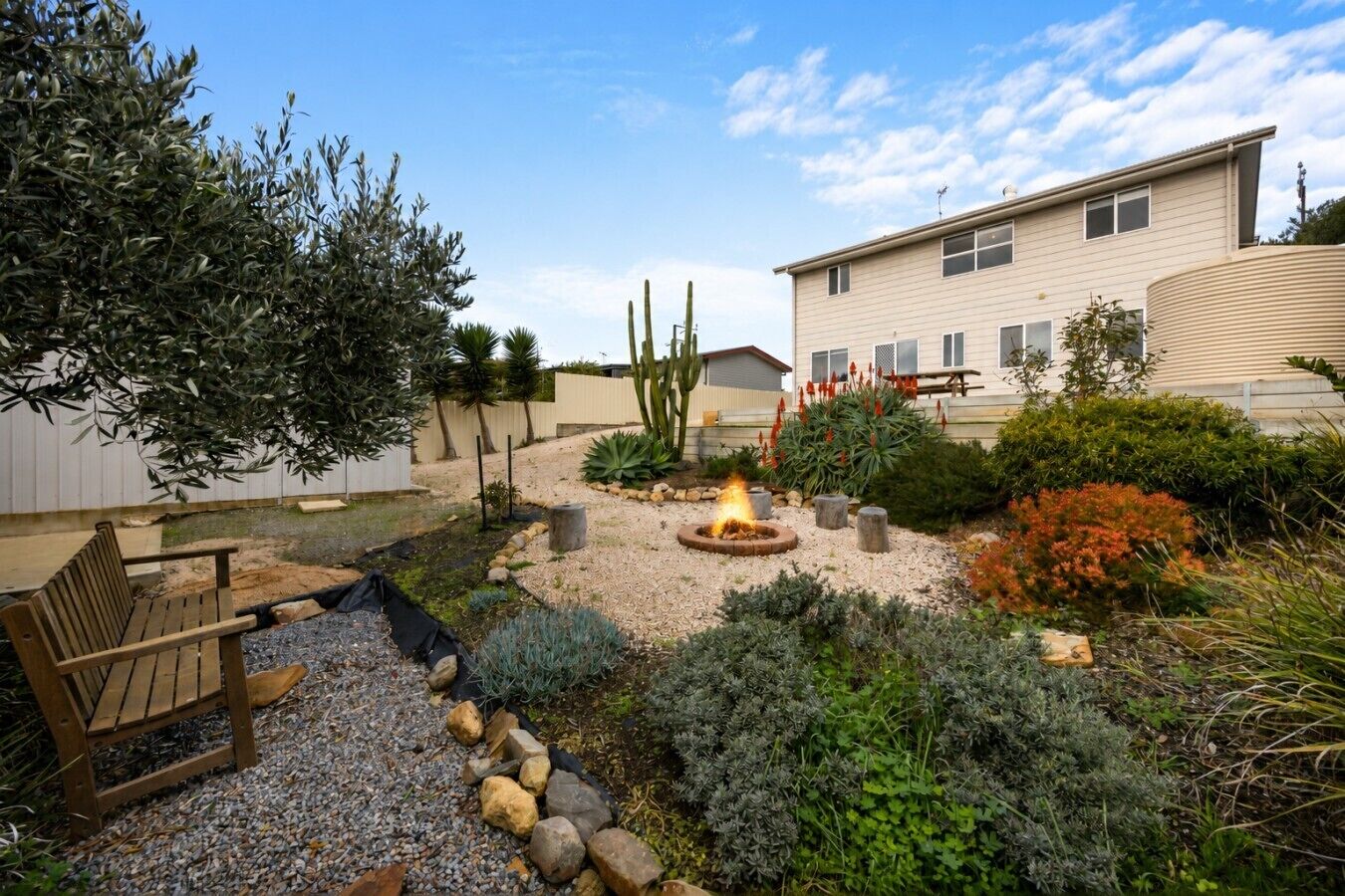 A landscaped backyard with a fire pit, a wooden bench, and various plants.