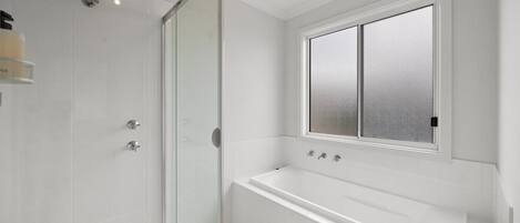 Un baño moderno con cabina de ducha de vidrio, bañera y ventana esmerilada.