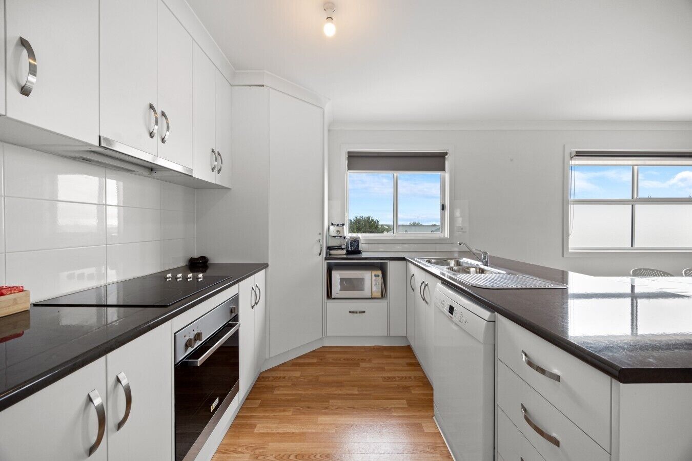 A modern kitchen with white cabinets, a black countertop, a built-in oven, a microwave, and a window providing a view.