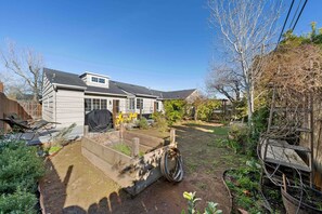 Ein Wohngrundstück mit erhöhten Blumenbeeten, einem Grill und einer Holzterrasse.