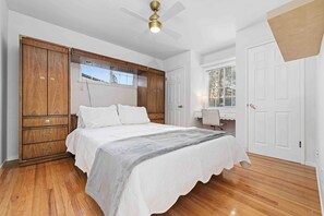 Ein Schlafzimmer mit Bett, Holzschrank, Deckenventilator und einem Fenster mit Blick.