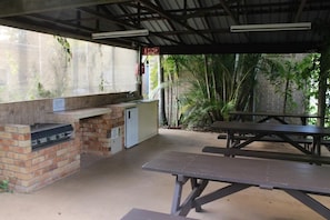 Un espace barbecue extérieur avec un gril en briques, un évier et une table de pique-nique.
