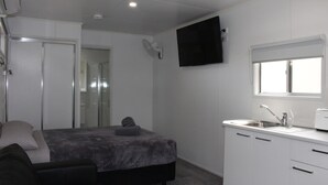 Una habitación pequeña con cama, mesita de noche y televisor en la pared.
