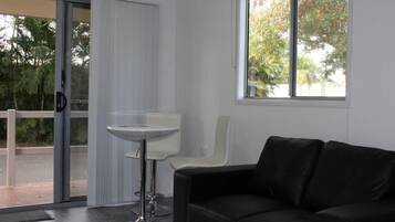 A modern room with a black leather sofa, a white table, and a sliding glass door leading to an outdoor area.