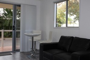 A modern room with a black leather sofa, a white table, and a sliding glass door leading to an outdoor area. - Huntsville Caravan Park (Maryborough)