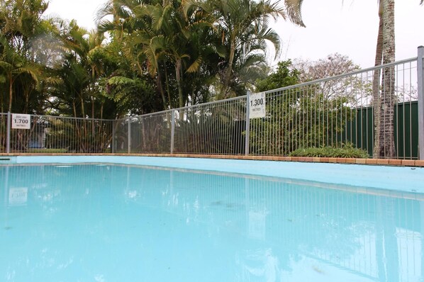 A swimming pool with a metal fence, surrounded by palm trees. - Huntsville Caravan Park (Maryborough)