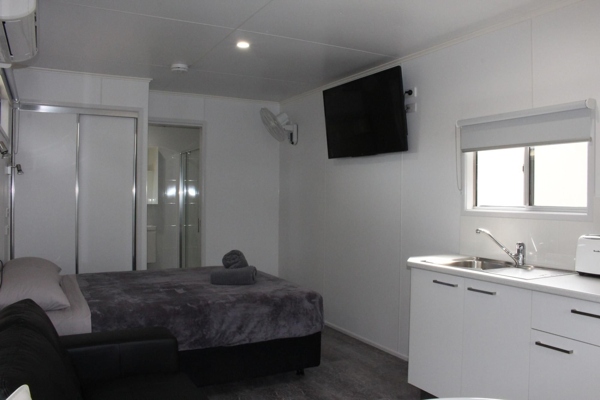 A compact bedroom with a bed, bedside table, and a TV mounted on the wall.