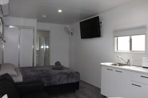 Quarto compacto com cama, mesa de cabeceira e televisão na parede.