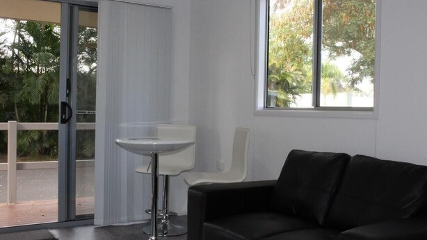 Una habitación moderna con un sofá de cuero negro, una mesa blanca y un ventanal corredero que da a un espacio exterior.