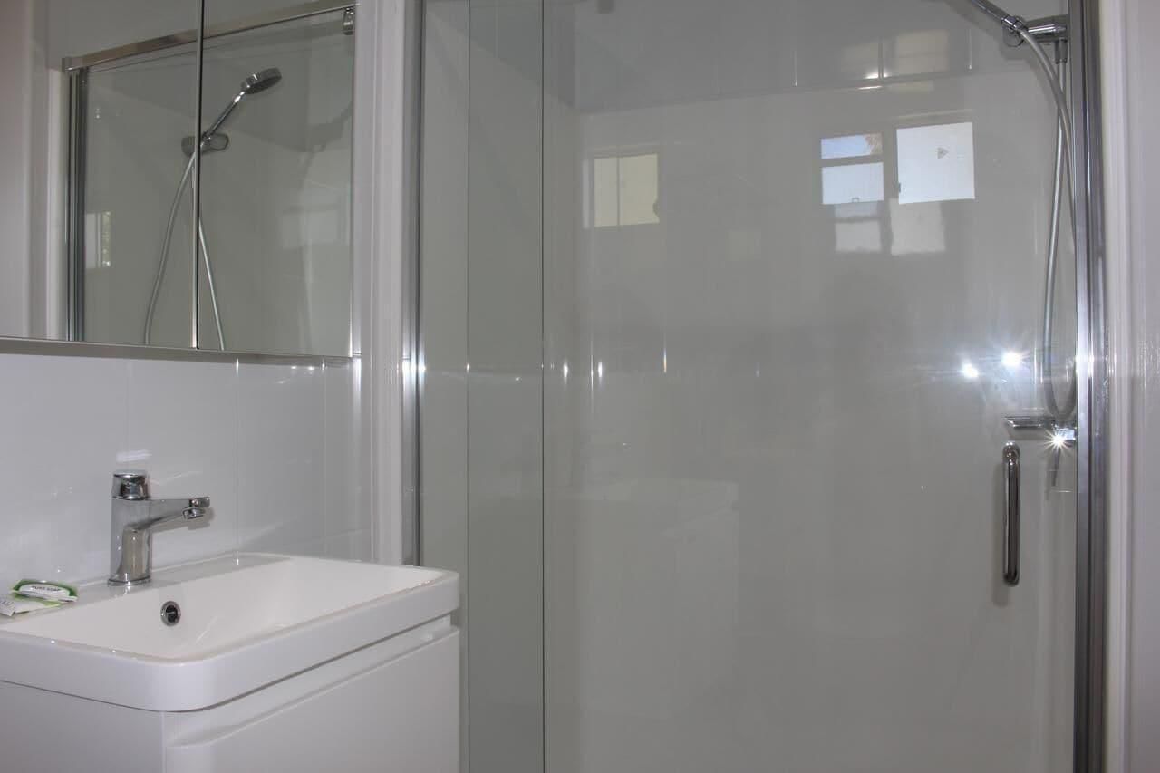 Een badkamer met een glazen douchecabine, een witte wastafel en een spiegel boven de wastafel.