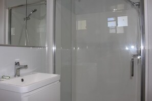 Un baño con cabina de ducha de vidrio, un lavabo blanco y un espejo sobre el lavabo.