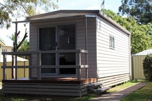 Una casa móvil pequeña de un solo piso con un porche, una puerta corredera y una ventana.