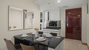 A modern kitchen with a dining area, including a glass table, chairs, and a vase with flowers. - Ardin by Kozystay - MERR (Surabaya)