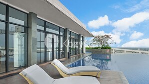 A modern infinity pool with lounge chairs, large windows, and a view of the sea. - Ardin by Kozystay - MERR (Surabaya)