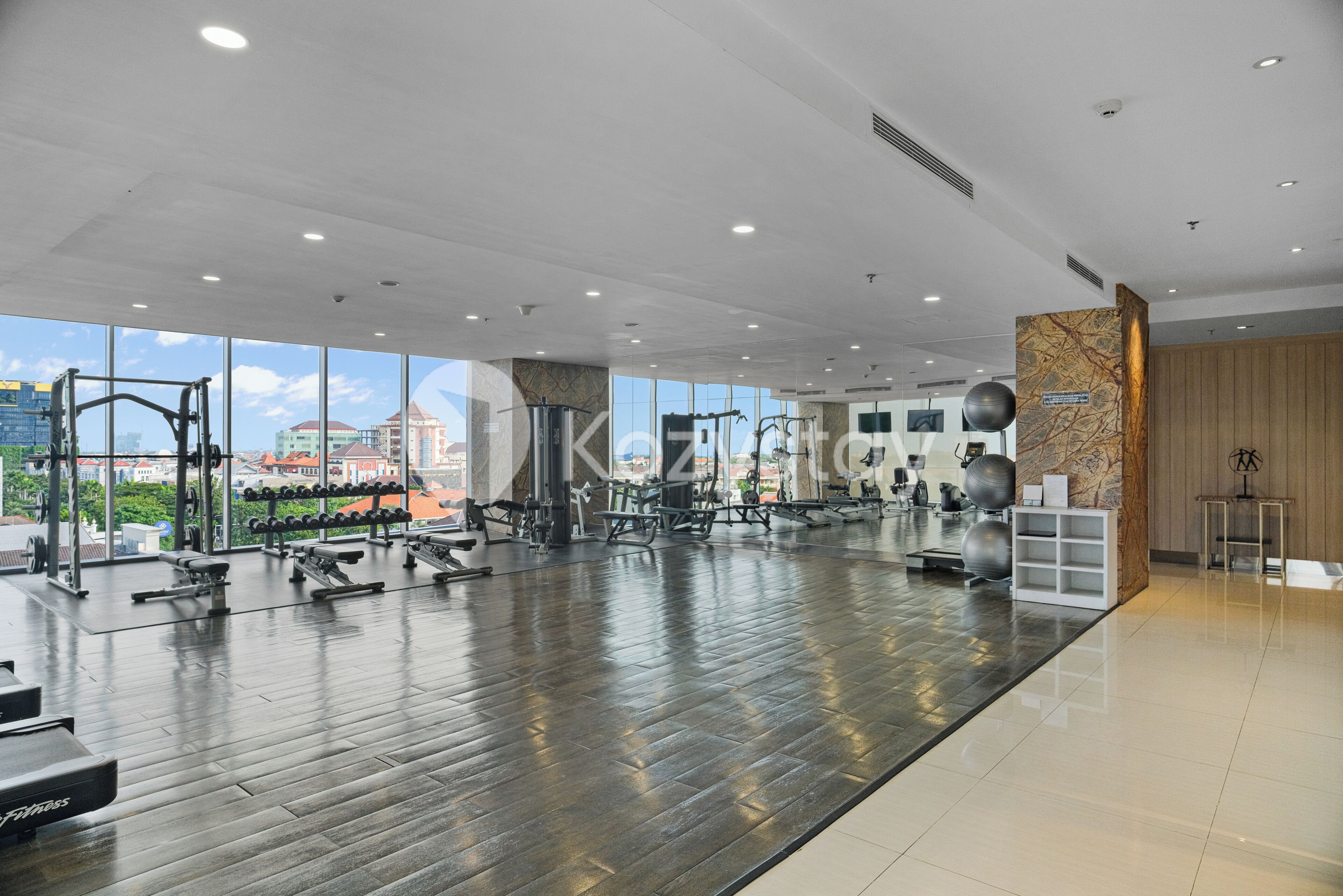 A modern gym with exercise equipment, large windows, and a view of buildings.