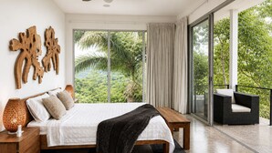 Een moderne slaapkamer met een groot bed, een houten hoofdbord en uitzicht op weelderige begroeiing doorgaande ramen van de vloer tot het plafond.