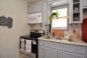 A kitchen with a stove, microwave, double sink, and cabinets.