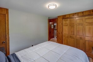 A bedroom with a bed, wooden wardrobe, and a door leading to a hallway. - Rustic Wilson Bay Cabin on Gull Lake | Beach & Dock (Nisswa)