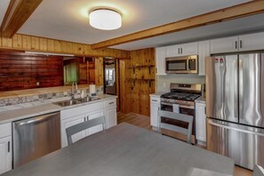 A modern kitchen with wooden paneling, stainless steel appliances, and a central island. - Rustic Wilson Bay Cabin on Gull Lake | Beach & Dock (Nisswa)