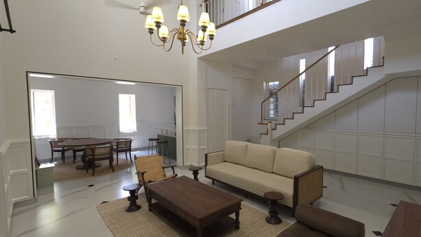 A spacious living area with a sofa, coffee table, and dining table. A staircase leads to an upper level.